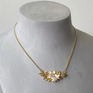 Guldhalsband med blommotiv - Säljer ett elegant guldhalsband med ett vackert blommotiv i mitten. Halsbandet har en fin kedja och blommorna är dekorerade med små gnistrande stenar. Perfekt för att ge en touch av glamour till vilken outfit som helst! Okänd metall 