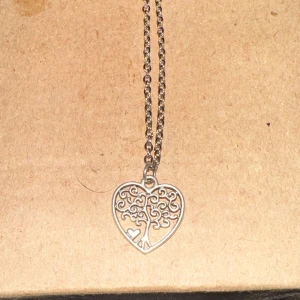 Halsband med hjärtformat trädmotiv - Säljer ett superfint halsband med ett hjärtformat hänge som har ett intrikat trädmotiv. Halsbandet är i silverfärg och kedjan är av medellängd. Perfekt för att ge en elegant touch till vilken outfit som helst!