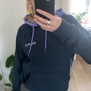 Mörkblå hoodie från Dickies - Säljer en snygg och bekväm mörkblå hoodie från Dickies i storlek XS. Den har en kontrasterande ljuslila huva. Perfekt för en avslappnad stil och passar bra till både höst och vår. 