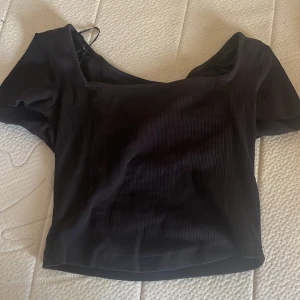 Svart ribbad topp från Bik Bok - Säljer en snygg svart ribbad topp från Bik Bok. Den har en stilren design med korta ärmar och en fyrkantig halsringning. Perfekt för både vardag och fest!