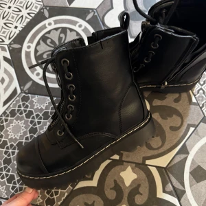 Svarta kängor med snörning och dragkedja - Snygga svarta kängor i fejkskinn med både snörning och dragkedja för enkel på- och avtagning. Perfekta för höst och vinter med en robust sula som ger bra grepp. Stilrena och passar till många olika outfits.