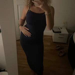 Mörkblå långklänning - Säljer en mörkblå långklänning med smala axelband som korsas i ryggen. Klänningen sitter tajt och formas efter kroppen💙