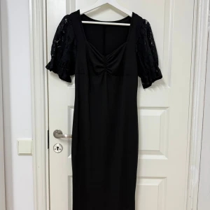 Svart klänning med spetsärmar - Elegant svart klänning med v-ringad design och puffiga spetsärmar. Perfekt för festliga tillfällen. Klänningen har en smickrande passform och är knälång. Materialet är mjukt och bekvämt, vilket gör den idealisk för både dag och kväll. Helt ny, oanvänd och redo för en fantastisk ny ägare!