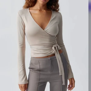 Beige omlottopp - Snygg beige omlottopp med långa ärmar och knytning i midjan. Perfekt för både vardag och fest, samt som en träningstopp. Strl M men passar även S