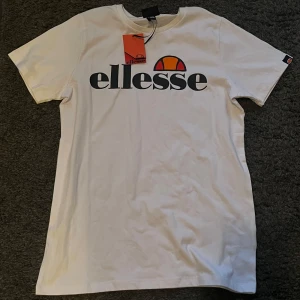 Vit t-shirt från Ellesse - Säljer en snygg vit t-shirt från Ellesse i nytt skick. Den har en ellesse logga på bröstet. Perfekt för en casual look eller träning. Kortärmad och i mjukt bomullsmaterial. Aldrig använd och prislappen finns kvar. Storlek 158/164 (13-14 år)