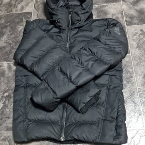 Adidas jacka - Säljer en svart dunjacka från Adidas i mycket bra skick. Jackan har en praktisk huva och dragkedja framtill. Perfekt för kalla vinterdagar. Nypris 1100kr