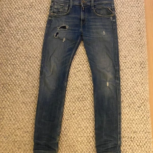 Blå Replay Anbass Jeans - Säljer ett par snygga blå jeans från Replay i modellen Anbass. De har är slim fit och är i bra skick med slitningar på framsidan. Modellen är väldigt populär och säljs inte längre. Tveka inte på att höra av er vid frågor.