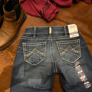 Ariat R.E.A.L Mid Rise original Bootcut jeans w27/L - Helt nya jeans från ariat, endast provade.  Alla taggar kvar.  Ett av deras populäraste modeller i färgen spitfire, storlek w27/L (long)💙 Slutsålda i alla storlekar på hemsidan, säljer endast då de var för långa för min smak.  Väldigt true to size med en bra passform, ett par jeans som passar till varje moment i vardagen.  Finns inte många ariat jeans i andrahandsmarknaden då de är så omtyckta😚