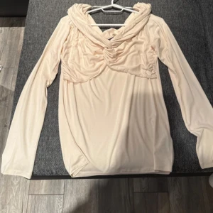 Beige långärmad topp från Gina Tricot - Säljer en superfin beige långärmad topp från Gina Tricot. Den har en unik draperad design vid halsen som ger en elegant touch. Perfekt för både vardag och fest! 🥰