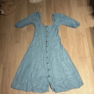Blå klänning med knappar - Säljer en söt blå klänning med knappar hela vägen ner. Den har korta ärmar och en v-ringad design. Perfekt för vår och sommar! 💙