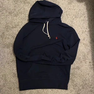 Mörkblå hoodie Polo Ralph Lauren - Säljer en stilren mörkblå hoodie från Polo Ralph Lauren i storlek S. Den har en klassisk design med en liten röd logga på bröstet och vita snören vid huvan. Perfekt för höst och vinter men även sommar. 