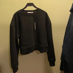 Svart croppad tröja från 157 - Säljer en svart tröja från 157 i storlek XS. Den är i nytt skick och har en enkel, stilren design med långa ärmar och rund hals. Perfekt för höst och vinter, och passar till alla tillfällen. Skön och bekväm att ha på sig! HELLT NY 