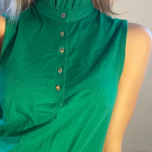 Grön ärmlös topp med knappar - Snygg grön ärmlös topp med hög krage och knappar framtill. Toppen har en enkel men stilren design som passar till både jeans och kjol.