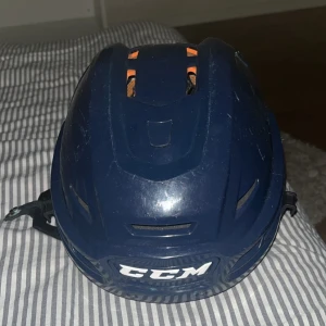 Blå hockeyhjälm från CCM - Säljer en blå hockeyhjälm från CCM i bra skick. Hjälmen har justerbara remmar och en vadderad insida för extra komfort och skydd. Perfekt för hockeyträning eller match. Ena öronskyddet har en spricka, inget som syns så mycket och går att byta. Passar de flesta huvudstorlekar och är lätt att justera för optimal passform.