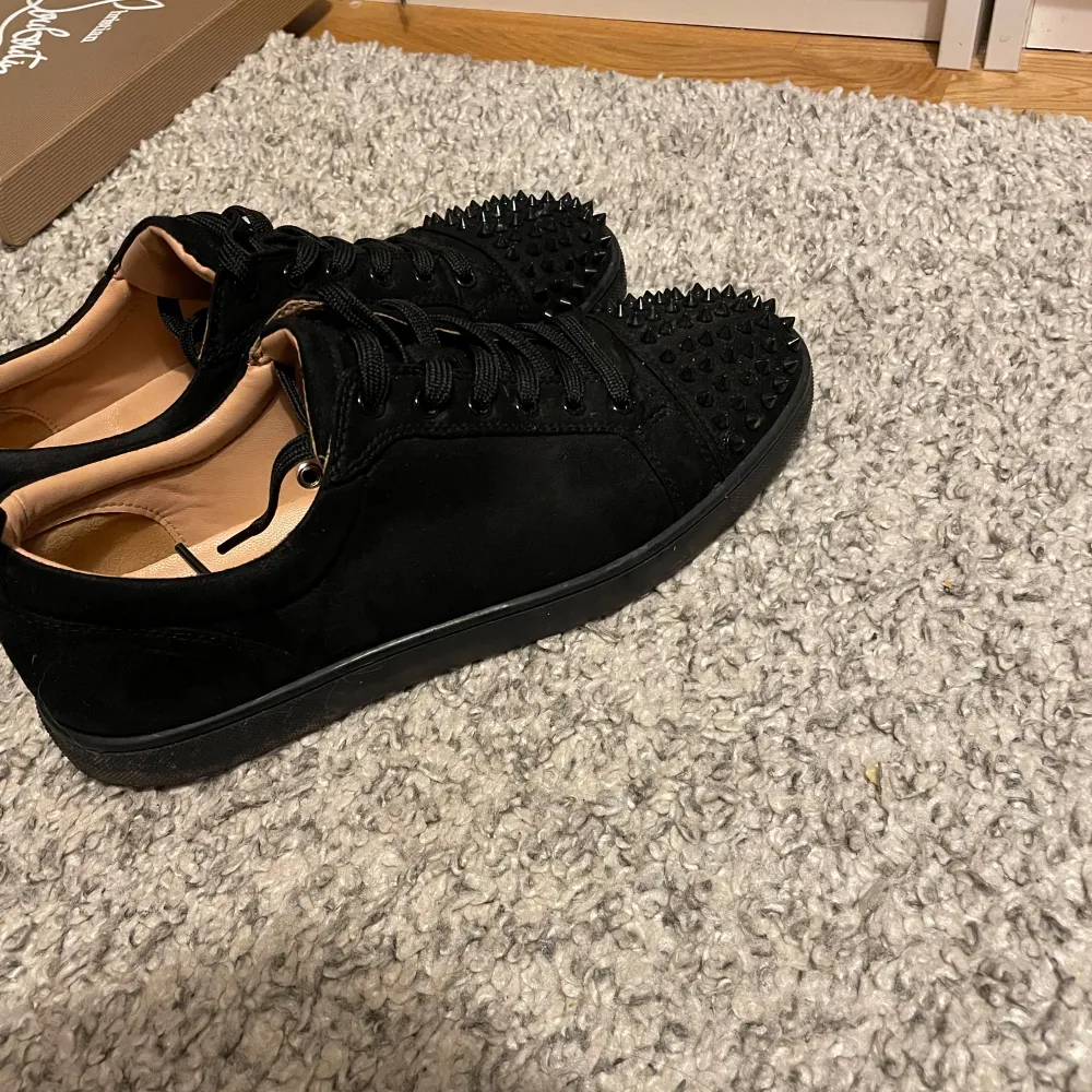 Säljer ett par svarta Louboutin sneakers i mycket bra skick. De har en cool design med nitar på ovansidan och den ikoniska röda sulan. Perfekta för att ge din outfit en edgy touch. Skorna kommer med originalförpackning och dustbag. Saknas en spik men det märks inte ens milt smutsiga för använda fåtal gånger därför är priset lågt . Skor.