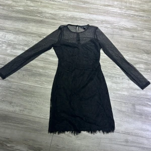 Svart spetsklänning från New Look - Snygg svart spetsklänning från New Look med långärmad design och transparenta detaljer. Perfekt för festliga tillfällen! Klänningen har en elegant passform och är gjord i ett mjukt spetsmaterial som ger en lyxig känsla.  Aldrig använd.
