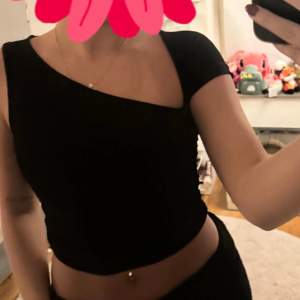 Snygg svart oneshoulder topp som är perfekt för en utekväll eller fest. Den har en tight passform och är croppad, vilket ger en trendig look. Toppen är ärmlös på ena sidan och har en kort ärm på andra, vilket gör den unik och stilren.