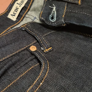 Mörkblå jeans från Acne - Säljer ett par snygga mörkblå jeans från Acne i storlek 26/32. De är i ett klassiskt snitt med dragkedja och knapp framtill. Materialet är 98% bomull och 2% elastan, vilket ger en skön passform. Perfekta för både vardag och fest! Väldigt sparsamt använda. Low raise och rak modell.