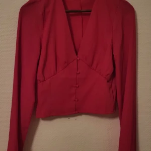 Blus mörkrosa - En vacker mörkrosa blus med djup ringning och trumpet ärmar. Knappar framtill. Bilden ger ingen rättvisa för färgen.