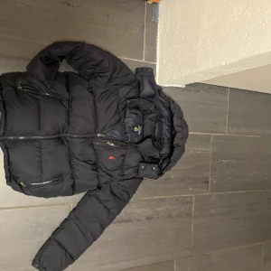 Svart dunjacka från Ralph Lauren - Säljer en snygg svart dunjacka från Ralph Lauren i mycket bra skick. Jackan har en praktisk huva och dragkedja framtill. Perfekt för kalla vinterdagar med sin varma och quiltade design. Två fickor med dragkedja för säker förvaring. Passar perfekt för både vardag och lite finare tillfällen. 14-16 i barnstorlek 