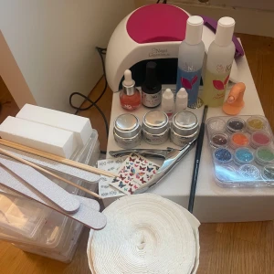 Nagelvårdspaket med UV-lampa och dekorationer - Komplett nagelvårdspaket med UV-lampa, nagelgeléer, färgglada dekorationer och verktyg. Inkluderar nagelrengöring, pensel, filar, buffertar och träpinnar. Perfekt för att skapa snygga nageldesigner hemma. Innehåller även nageltippar i olika storlekar och fjärilsdekaler för extra stil. (Gelerna är använda men finns produkt kvar)