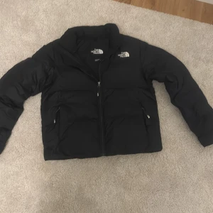 Svart dunjacka från The North Face - Säljer en svart dunjacka från The North Face i mycket bra skick. Jackan har en dragkedja framtill och två praktiska fickor med dragkedjor. Perfekt för kalla vinterdagar och höstpromenader. Den är både stilren och funktionell! Nypris är mellan 2500-3000 mitt pris är 1200 tveka inte att höra av dig vid minsta fundering :)