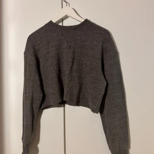 Grå croppad stickad tröja - Säljer en superfin grå croppad stickad tröja. Perfekt för höst och vår med sin mysiga och stilrena look. Tröjan har långa ärmar och en enkel design som passar till allt. Perfekt för lager-på-lager eller som den är. 🖤