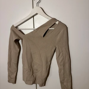 Beige offshoulder tröja - Säljer en snygg beige offshoulder tröja i ribbat material. Perfekt för både vardag och fest! Tröjan har långa ärmar och en unik design med en asymmetrisk axel. Superbekväm och stilren, passar till allt från jeans till kjol. Hör av dig vid intresse! ✨