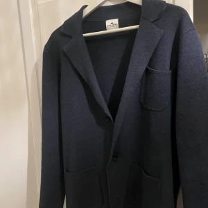 Mörkblå kavaj från John Henric - Säljer en stilren mörkblå kavaj från John Henric i storlek S. Perfekt för både vardag och fest. Kavajen har en klassisk design med tre knappar och fickor fram. Den är i mycket bra skick!