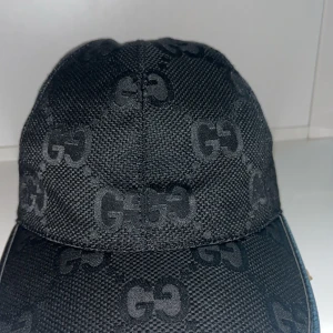 Svart keps  - Snygg svart keps med monogrammönster. Perfekt för att ge din outfit en lyxig touch. Kepsen har en klassisk design med böjd skärm och justerbar passform. Passar både till vardags och festliga tillfällen.