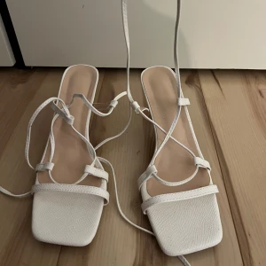 Vita sandaler med snörning - Säljer ett par stilrena vita sandaler med snörning. De har en fyrkantig tå och en elegant design som passar perfekt för sommarens alla fester. Sandalerna är i mycket bra skick och har en liten klack för extra stilpoäng. Storlek 39. Aldrig använda bara stått och dammat (fixar såklart vid försäljning).