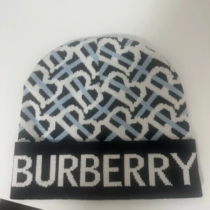 Burberry mössa - Snygg mössa från Burberry med ett coolt mönster i svart, vitt och blått. Den har en bred kant med Burberry-loggan i vitt. Perfekt för att hålla sig varm och stilren under kyliga dagar. One size