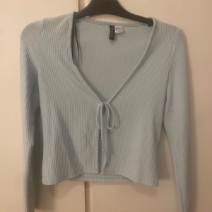 Ljusblå ribbad tröja med knyt - Säljer en superfin ljusblå ribbad tröja med knyt framtill. Den har en v-ringad design och är lite croppad, vilket gör den perfekt för både vår och sommar. Använd mycket men i bra skick!🩵
