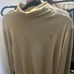 Beige polotröja från Ralph Lauren - Säljer en stilren beige polotröja från Ralph Lauren. Tröjan har en klassisk design med långärmad passform och det ikoniska broderade logotypen på bröstet. 
