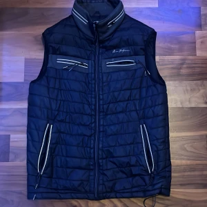 Svart quiltad väst från Remx Performance - Säljer en svart quiltad väst från Remx Performance i storlek S. Västen har en dragkedja framtill och flera praktiska fickor med dragkedjor. Perfekt för höst och vår när du vill hålla dig varm men ändå ha rörelsefrihet. Passar både till vardags och för utomhusaktiviteter.