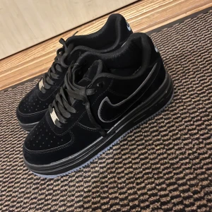 Svarta Nike sneakers - Säljer ett par svarta Nike sneakers i mycket bra skick. De har en stilren design med snörning och en diskret Nike-logga på sidan. Perfekta för både vardag och träning. Skorna är bekväma och har en bra passform.