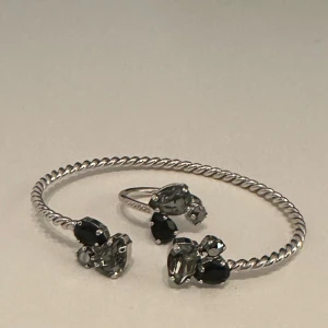 Silverfärgat armband och ring med svarta och klara stenar - Matchande ring och armband från Caroline Svedbom som är helt oanvända. Nypris för armbandet 795 kr och nypris för ringen 495. Både armbandet och ringen är justerbara så passar vem som helst! Pris i annonsen är för båda! Jag har sänkt priset från 750 men säljer inte under 500. 