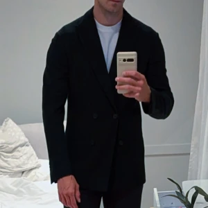 Marinblå dubbelknäppt kavaj från Boggi Milano stl 48 - Säljer en Marinblå dubbelknäppt kavaj från Boggi Milano stl 48 i mycket bra skick. Den har en mjuk stickad design med dubbelknäppning och fyra knappar på ärmarna. Perfekt för både formella tillfällen och vardagsbruk. Passar bra till höst och vinter. Modell är 183 cm och 77kg.