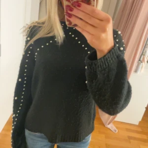 Svart tröja med pärldetaljer - Säljer en superfin svart tröja med pärlor längs ärmarna och axlarna. Den är perfekt för höst och vinter och har en mysig, stickad känsla. Tröjan har långa ärmar och en normal passform. Perfekt för att piffa upp vardagslooken eller till fest! 🖤