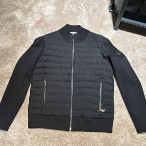 Svart jacka från Moncler - Säljer en snygg svart jacka från Moncler i mycket bra skick. Jackan har en quiltad framsida med dragkedja och långa ärmar. Perfekt för höst och vår. Den är gjord av polyester och har en stilren design med Moncler-logga på ärmen.