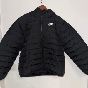 Svart pufferjacka från Nike - Säljer en svart pufferjacka från Nike i mycket bra skick. Jackan har en dragkedja framtill och är perfekt för höst och vinter. Den är långärmad och har en normal passform. Superbekväm och stilren för alla tillfällen! Litet hål i armen.
