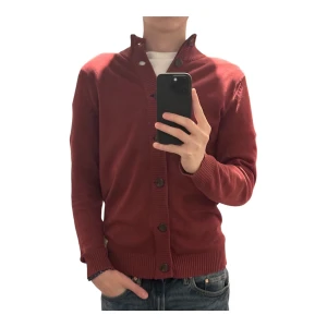 Röd kofta med knappar - Säljer en snygg röd kofta med knappar framtill. Den har en hög krage och ribbade muddar vid ärmslut och nederkant. Perfekt för höst och vinter, och funkar både till vardags och lite finare tillfällen. Passar bra med jeans, bara att höra av sig vid frågor och funderingar!