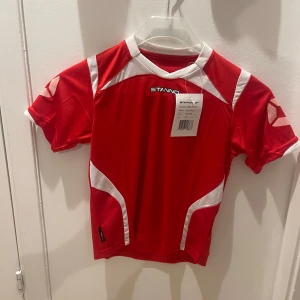 Röd och vit fotbollströja från stanno  - Snygg röd fotbollströja från Stanno med vita detaljer. Kortärmad design perfekt för träning eller match. Tillverkad i ett lätt och andningsbart material för optimal komfort.