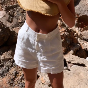 Vita linne shorts - Snygga vita shorts i linne med hög midja. Perfekta för en dag på stranden eller en somrig utflykt. De har en klassisk design med knapp och dragkedja framtill. 