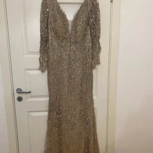 Glittrig långklänning med paljetter - Elegant långklänning i champagnefärg med glittriga paljetter och v-ringning. Klänningen har långa ärmar och en figurnära passform, perfekt för festliga tillfällen. Ordpris:3000 ‼️Använd endast en gång