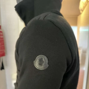 Moncler cardigan jacka - Moncler black lable med dragkedja och quiltad design. Den har en stilren look med Moncler-logga på ärmen.
