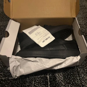 Svarta Nike Air Force 1 - Säljer ett par klassiska svarta Nike Air Force 1 sneakers. Skorna har en stilren design med snörning och är tillverkade i skinn. Perfekta för en casual look. Har används en gång bara men ser fortfarande ut som nytt och kvitto samt box ingår. Hör av er vid intresse!