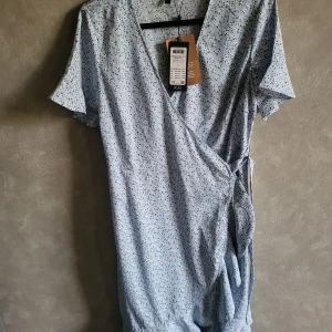 Blommig omlottkläning - Ljusblå blommig omlott klänning från Vero moda. Oanvänd med lapparna kvar