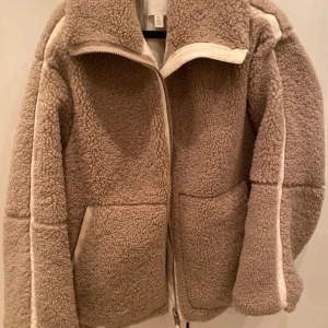 Beige teddyjacka H&M - Mysig beige teddyjacka med dragkedja och två framfickor. Perfekt för kyliga dagar med sin fluffiga och varma design. Jackan har en hög krage och långa ärmar för extra komfort. Slutsåld! Nyskick men lite smink på kragen, går bort i tvätten❤️