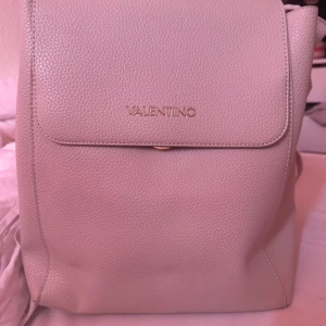 Beige ryggsäck från Valentino - Snygg och stilren beige ryggsäck från Valentino i skinn. Väskan har justerbara axelremmar och en praktisk dragkedja inuti för säker förvaring. Perfekt för en chic och elegant look.